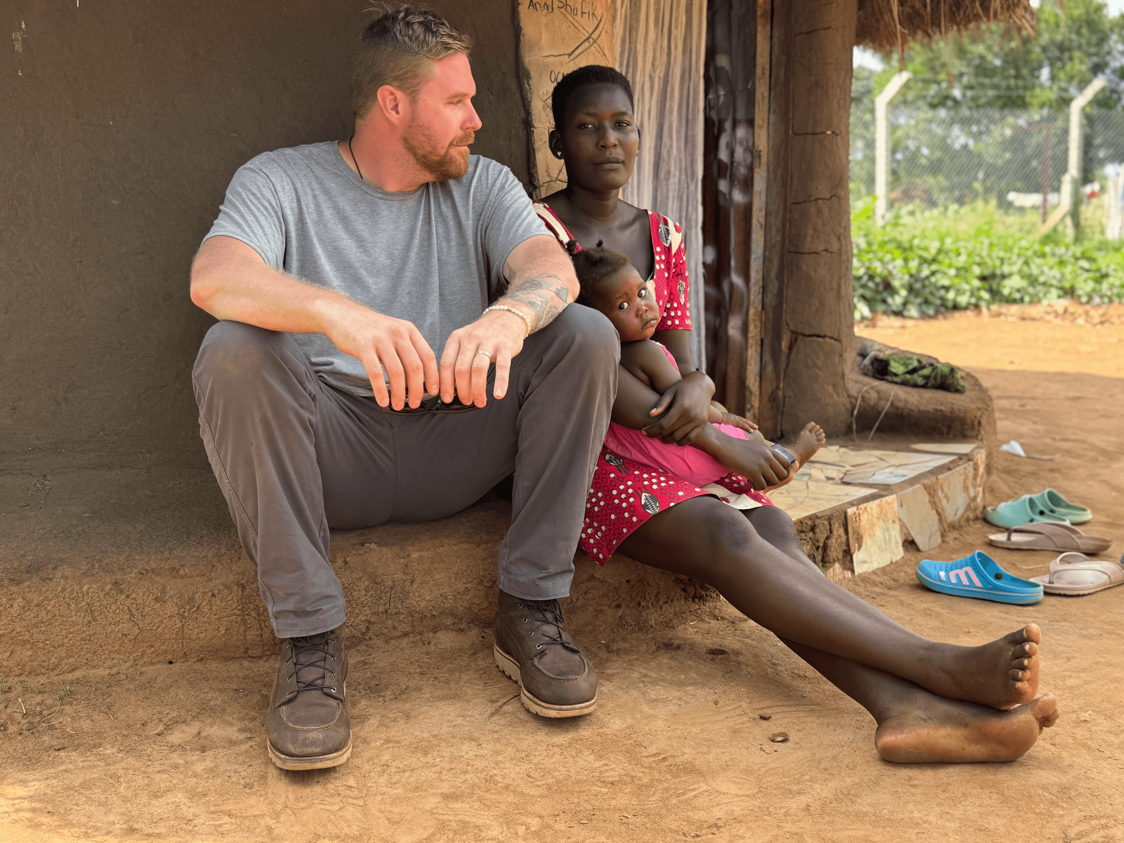 Kevin seated with a mother and child in Northern Uganda